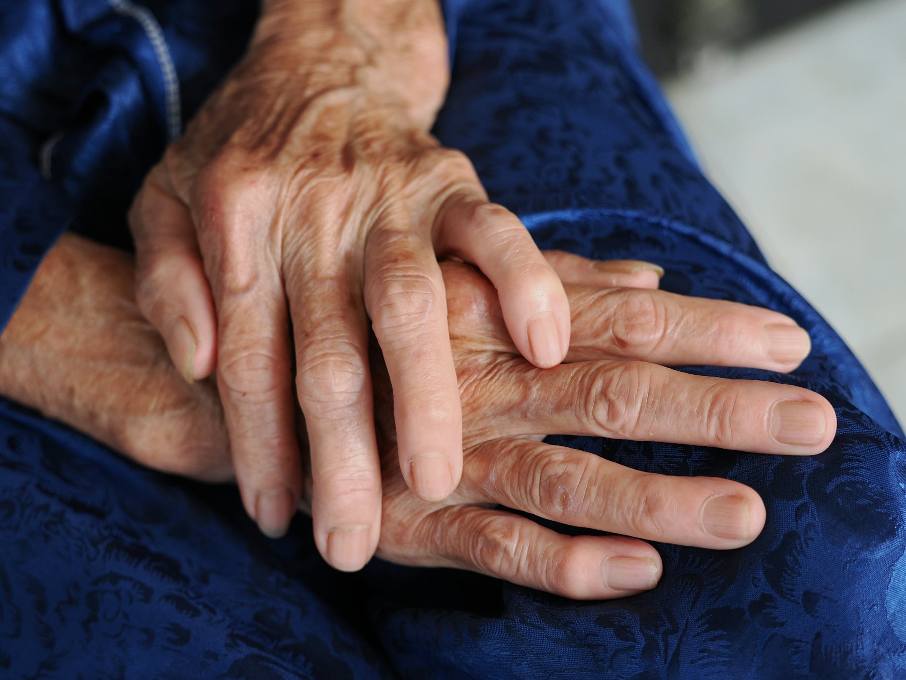 An older person's hands resting on blue fabric